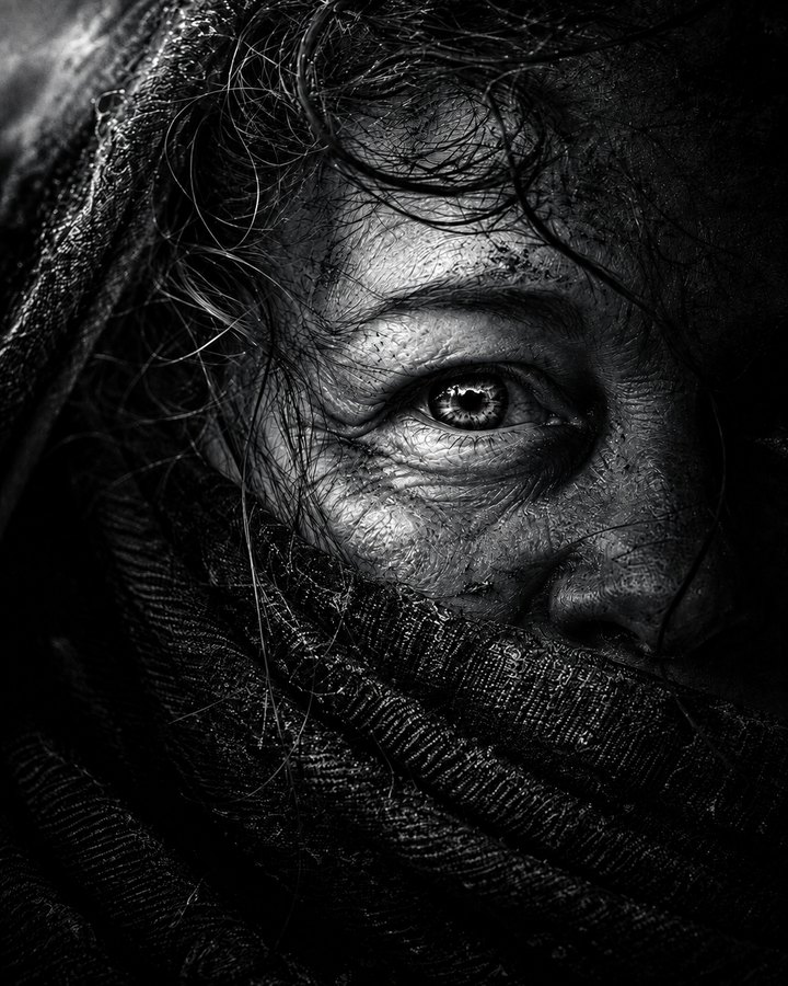 High-contrast silvertone close-up of a woman with one eye visible above a dark textured scarf, with loose hair and dust across her face.