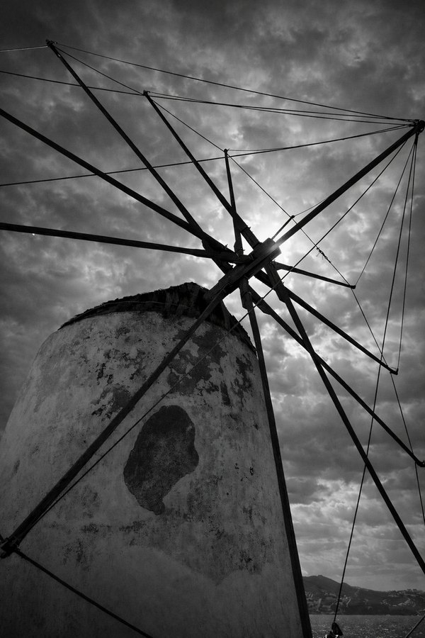 A weathered windmill is photographed in black and white beneath a dramatic cloud-filled sky.