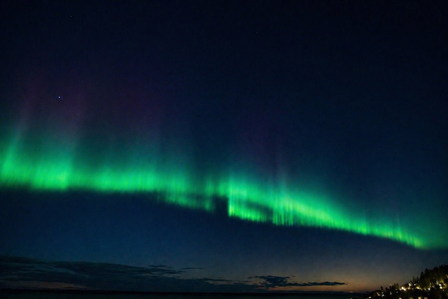Bright green aurora stretching across a dark night sky above a low, shadowed horizon.