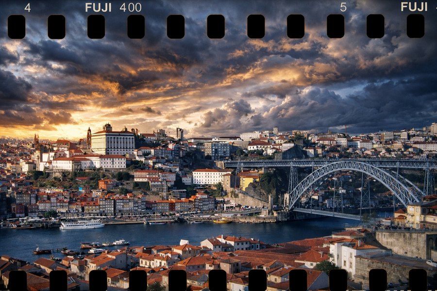 Panoramic film-frame view of Porto at sunset, with the Douro River, hillside buildings, and the Dom Luís I Bridge.