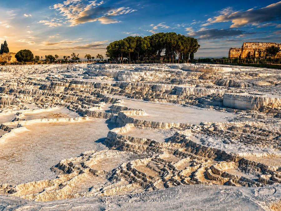 White mineral terraces and shallow pools stretching across a sunlit landscape beneath a blue sky.